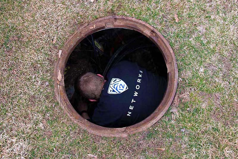 In this March 2016 file photo, Fiber Team Supervisor Destry Mulleneaux descends a manhole in the process of installing Air Blown Fiber (ABF) from the Energy and Geoscience Institute to the Dumke Health Professions Education building.