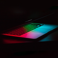 An open laptop computer reflects neon colors on its keyboard