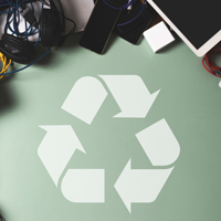 A faded white recycle icon below a pile of electronics.