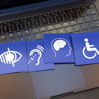 Four blue paper squares, each with a symbol or icon for a disability, lie on top of the keyboard of a laptop. The icons, from left, indicate sight, hearing, cognitive, and physical impairments.